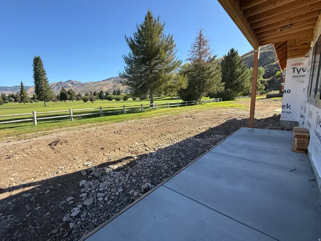 Expansive concrete patio with exposed wood ceiling beams, offering mountain scenery and a golf course backdrop
