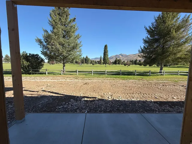 Expansive concrete patio with exposed wood structural beams, overlooking a manicured green space, a wooden fence, and distant mountains