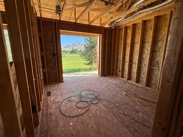 Framed interior with visible structural elements and a large portal opening to a green expanse and mountain backdrop