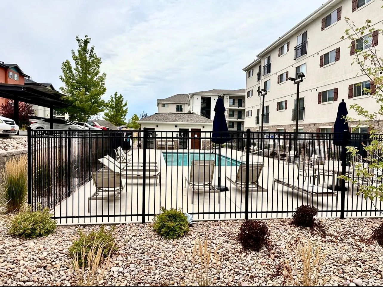 Outdoor swimming pool with surrounding fence, adjacent patio, and stone landscaping