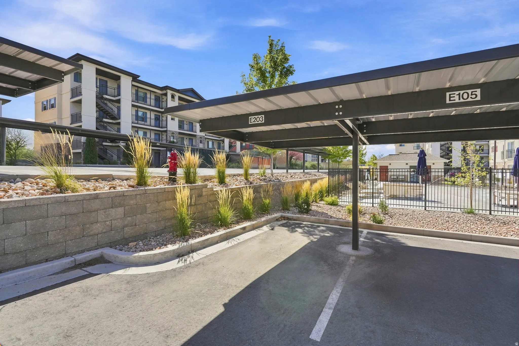 Covered parking area with designated spaces, concrete block retaining wall, and landscaped beds with ornamental grasses