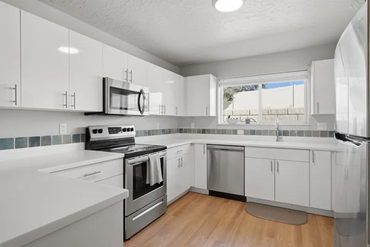 Kitchen featuring white cabinetry, stainless steel appliances, white countertops, a tiled backsplash, and wood-finish flooring