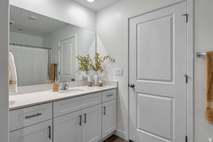 White vanity with a light countertop and undermount sink, large wall-mounted mirror, and recessed lighting
