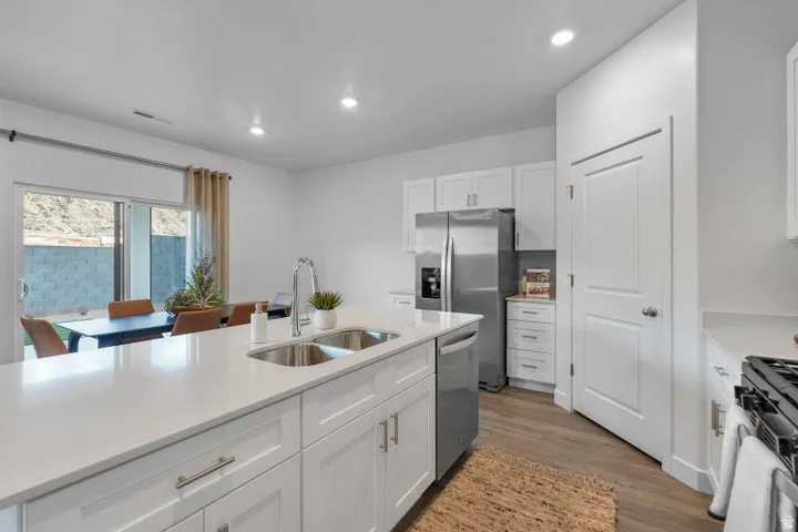 Kitchen featuring white shaker cabinetry, stainless steel appliances, a center island with double sinks, and wood-finish flooring