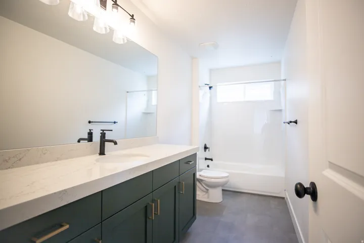 Full secondary bath with extra-long vanity, painted wood cabinets and quartz slab countertops.
