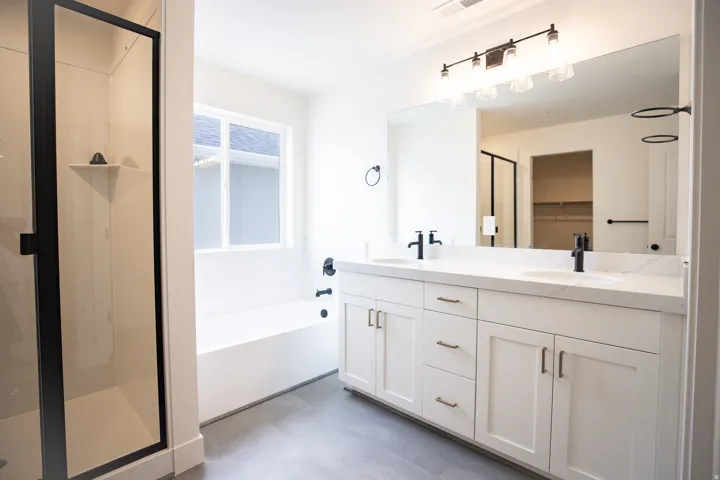 Primary bath with painted white wood cabinets, dual sinks, quartz slab countertops, soaker tub, walk-in shower, adjacent to large walk-in closet as part of primary suite.