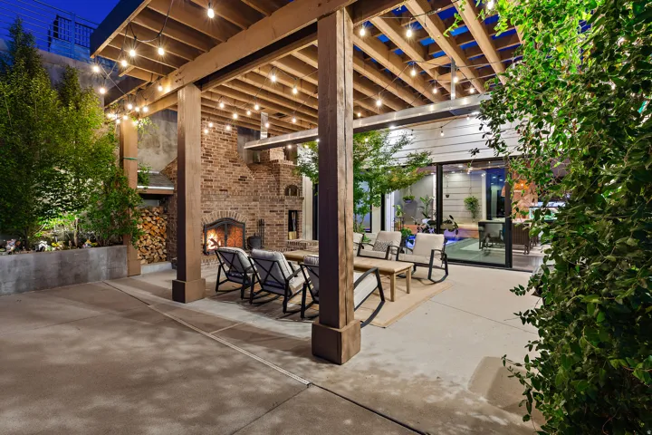 Expansive patio featuring a wood pergola, string lighting, a large brick fireplace, and mature landscaping
