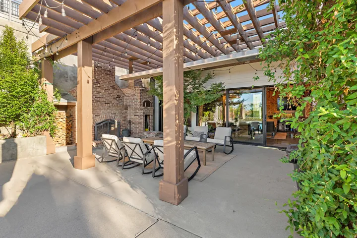 Expansive concrete patio featuring a wood-frame pergola, built-in brick fireplace, and integrated wood storage