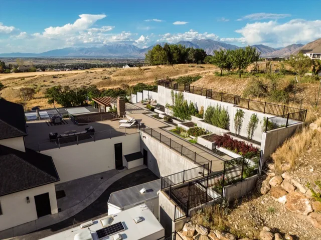 Multi-level concrete retaining walls with integrated planters, expansive upper-level patio, mountains in the distance, and established trees