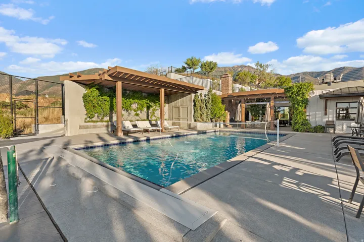 Swimming pool with integrated volleyball net, expansive concrete decking, and an adjacent wood pergola