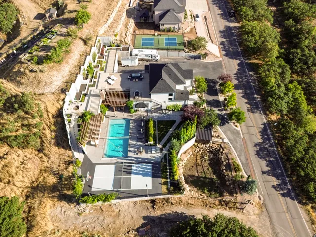 Expansive property featuring a swimming pool, multiple pergolas, a terraced retaining wall, and an outdoor court