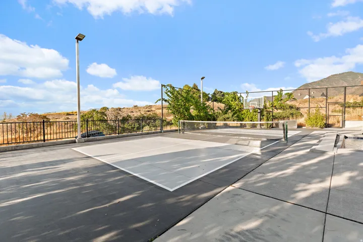 Outdoor sports court featuring a tennis net, basketball hoop, and perimeter fencing