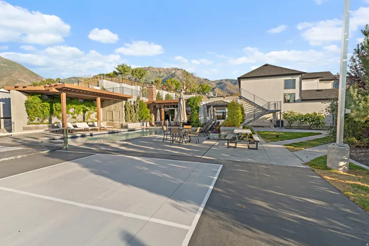 Outdoor recreational area featuring a swimming pool, wood pergola, paved court, and concrete pathways