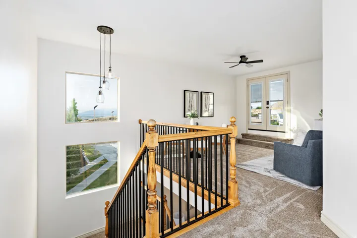 Staircase with wood balusters and black metal spindles, three square windows, three-light pendant fixture, carpeted landing, and double French doors