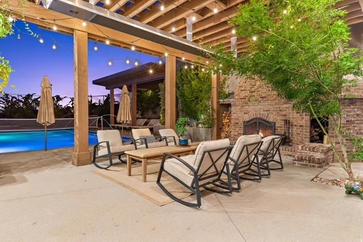 Outdoor living space featuring a swimming pool, stone patio, wood pergola, and a brick fireplace