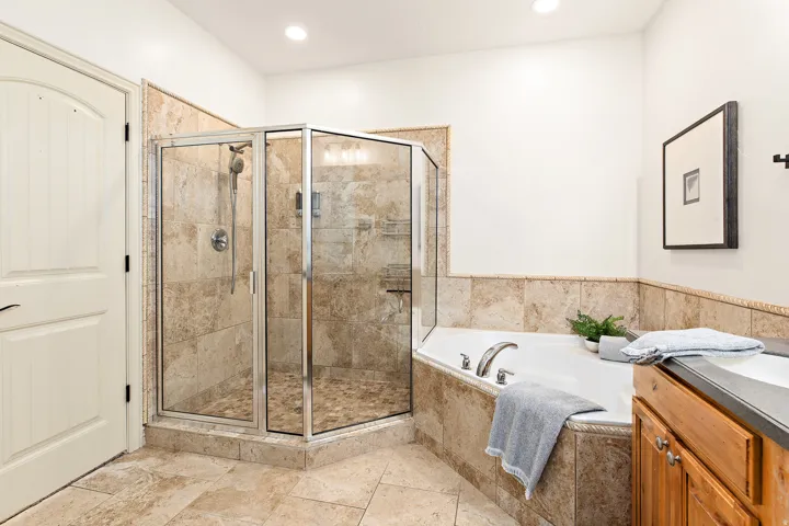 Glass-enclosed shower with stone tile surround, integrated soaking tub, wood vanity with built-in cabinetry, and stone tile flooring