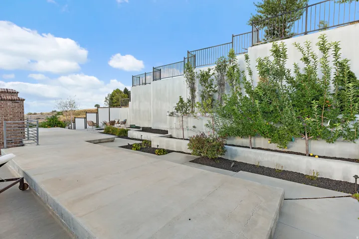 Multi-level concrete patio with integrated planters, mature greenery, and tiered retaining walls featuring black metal railings
