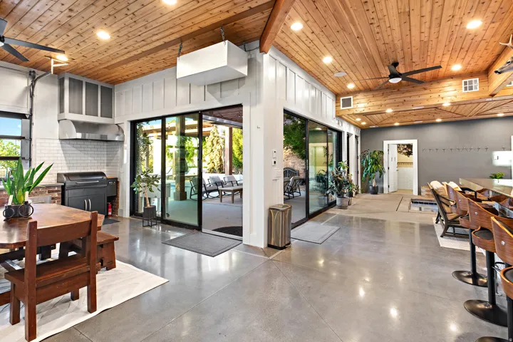 Wood-paneled ceilings with exposed beams, polished concrete flooring, extensive sliding glass doors, built-in kitchen area with white subway tile backsplash, and a large bar with built-in seating