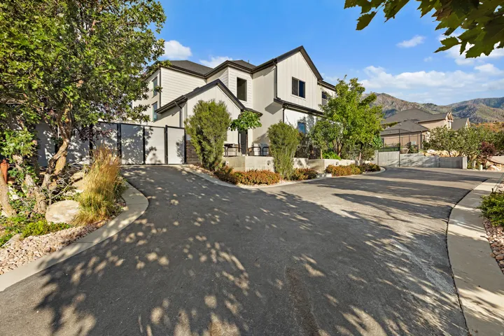 Contemporary exterior with vertical siding and dark trim, featuring an asphalt driveway, mature trees, and mountainous terrain in the background