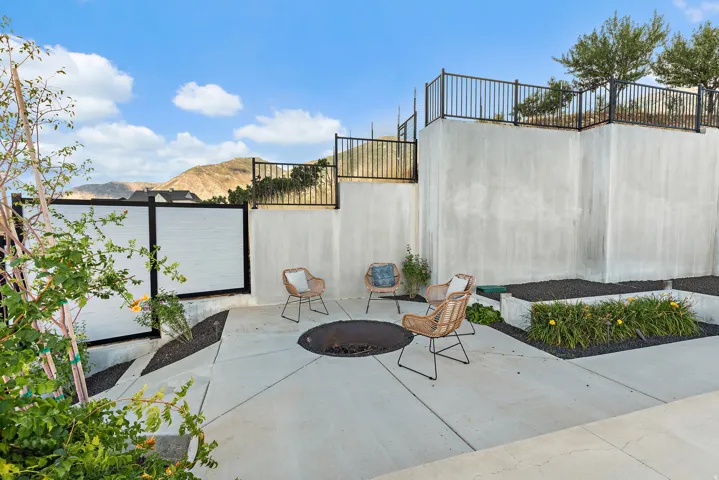 Outdoor patio area with concrete hardscaping, built-in fire pit, privacy fencing, and tiered landscaping