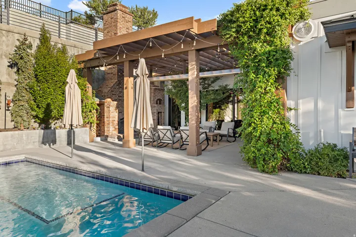 Swimming pool with blue tile border, concrete patio, and a wood pergola