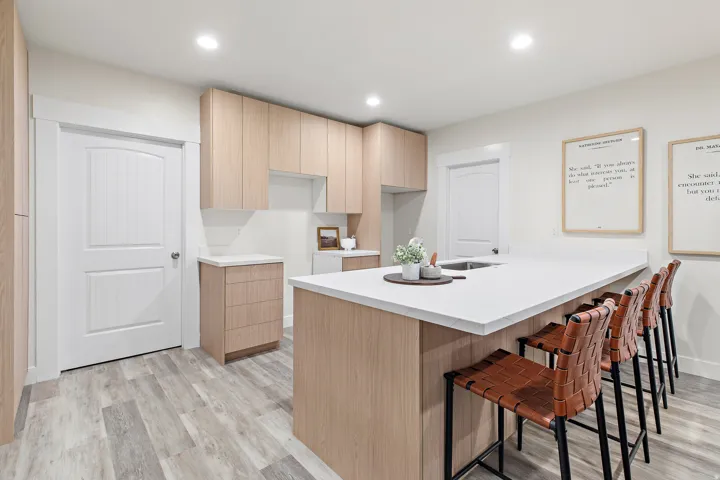 Contemporary kitchen featuring light wood-finish cabinetry, white countertops, a large island with sink, recessed lighting, and wood-finish flooring