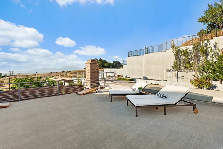 Expansive outdoor patio with tiered retaining walls, established landscaping, and a brick chimney feature