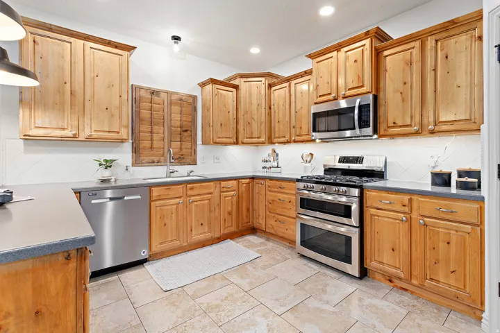 Wood-finish cabinetry, stainless steel appliances, modern tile backsplash, recessed lighting, and durable countertop surfaces