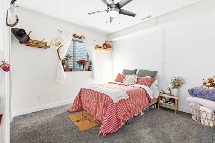 White shiplap accent wall, wall-to-wall carpeting, ceiling fan with integrated lighting, and a window with white drapes