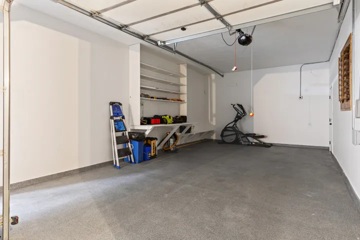 Spacious garage with an epoxy-coated floor, built-in shelving, a workbench, and a white overhead garage door