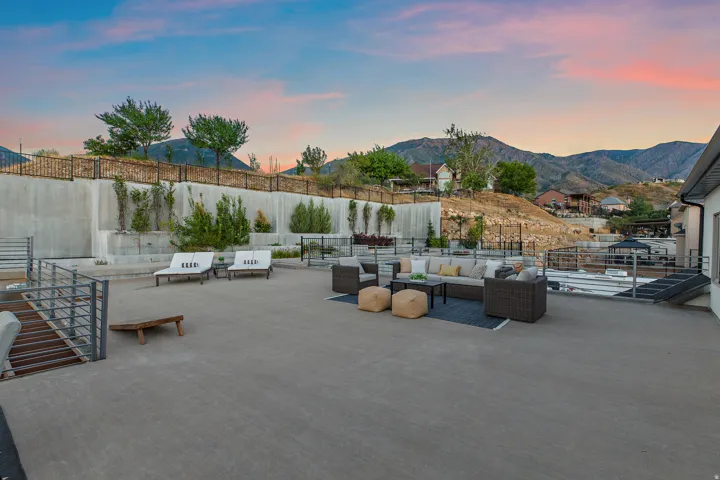 Expansive concrete patio with multiple defined seating areas, retaining walls with integrated landscaping, and metal railings