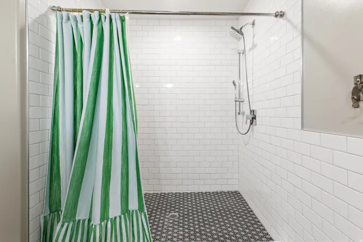 White subway tile shower walls, patterned shower floor tile, mounted shower head with handheld sprayer