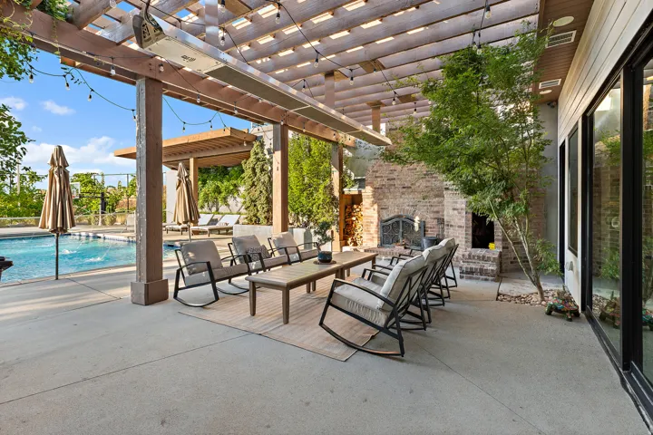 Expansive outdoor patio with a wooden pergola, string lighting, and an integrated outdoor fireplace