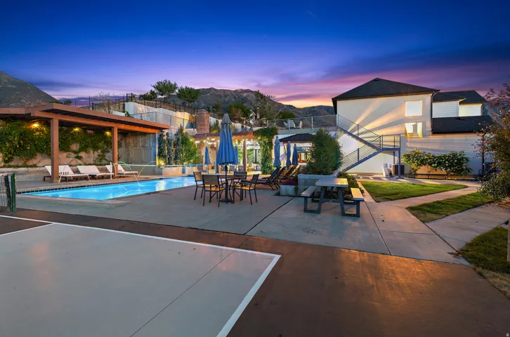 Resort-style pool with a wooden pergola, surrounding concrete patio, and a dedicated sport court
