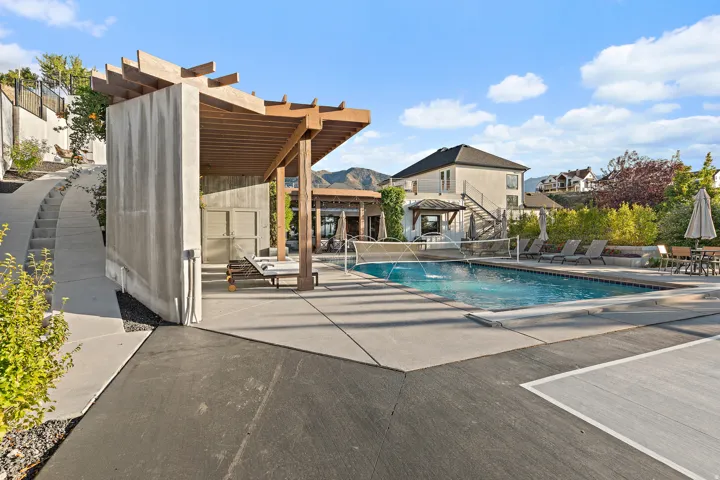 Outdoor swimming pool with integrated water features, expansive concrete decking, a substantial wood pergola, and a separate concrete structure with privacy screens