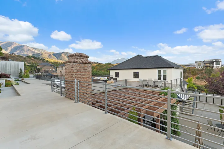 Expansive outdoor patio with a pergola, modern metal railings, brick pillar accents, and a large additional deck space