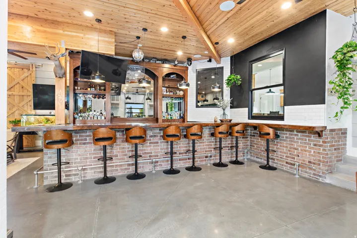 Vaulted wood-finish ceiling, brick-clad bar with wood-finish countertop, built-in shelving, concrete flooring, and an integrated window