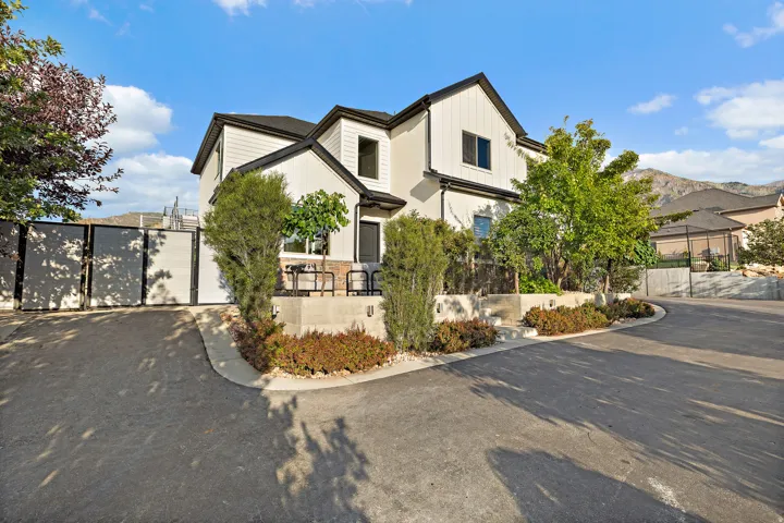 Modern facade with white siding and black trim, featuring a paved driveway, integrated planters with mature landscaping, and an exterior patio with seating