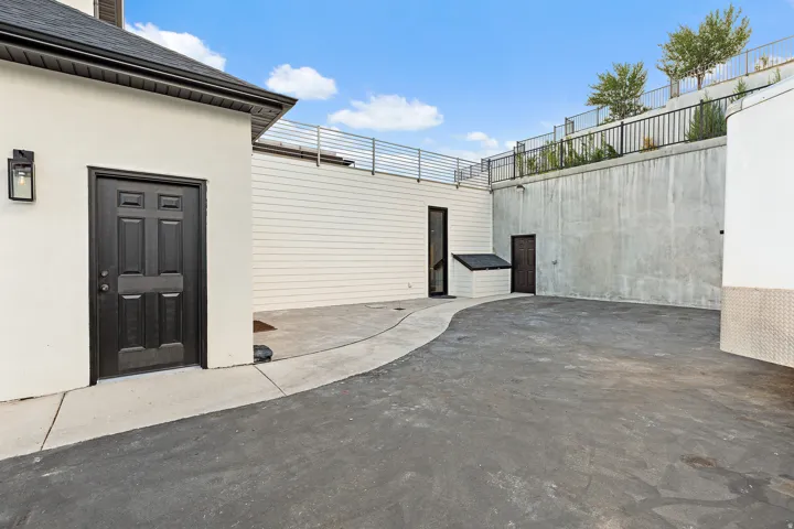 Paved outdoor space with a concrete pathway, white siding, and a dark entry door with exterior lighting
