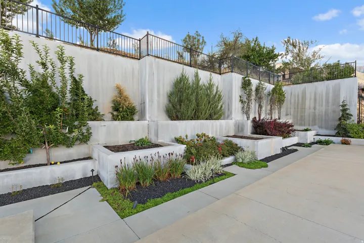 Tiered concrete retaining walls with integrated planters, black metal fencing, and mature landscaping