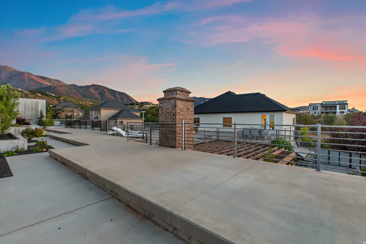 Expansive concrete patio with integrated planters, a brick chimney feature, and metal railings overlooking mountain scenery
