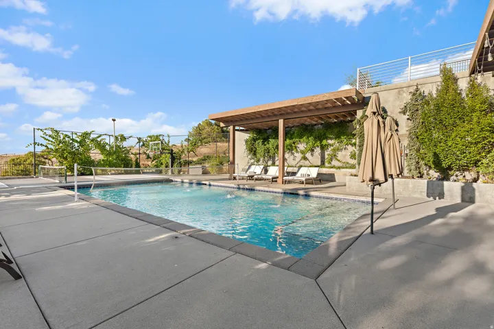 In-ground swimming pool, concrete patio, wood pergola, built-in planters, and concrete retaining wall