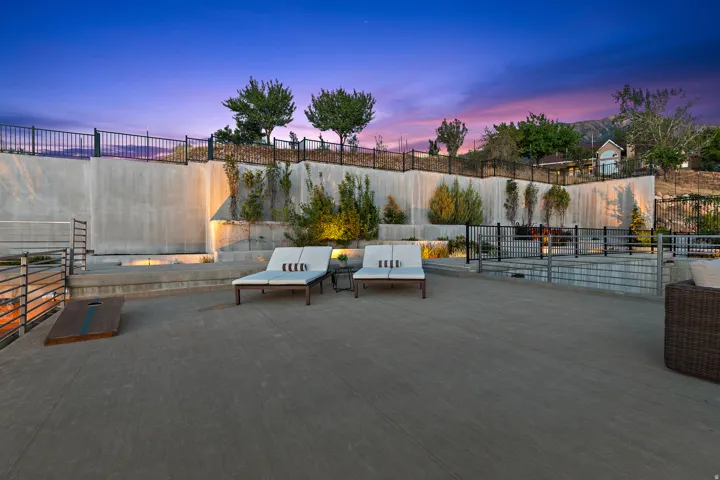 Expansive concrete patio with tiered retaining walls, integrated landscape lighting, and black metal fencing