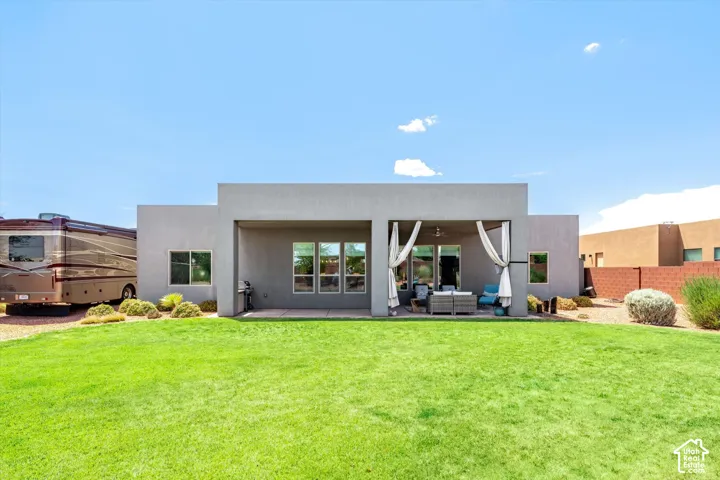 Expansive backyard with a manicured lawn, covered patio, multiple windows, and a gravel parking area