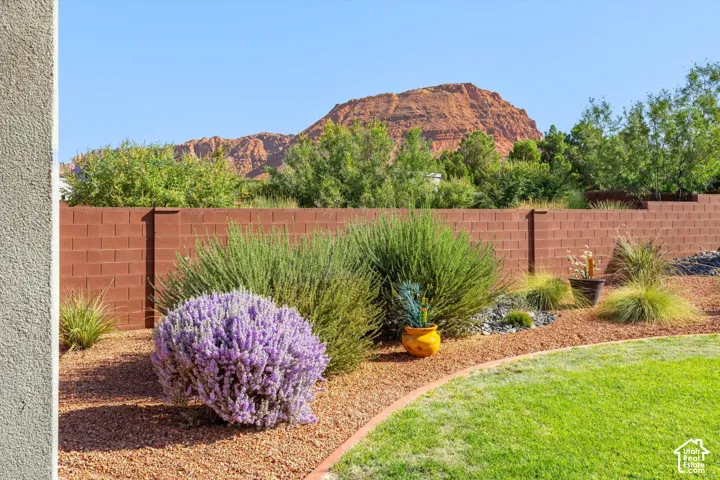 Manicured lawn with mature shrubs, reddish-brown block wall, and distant red rock formations