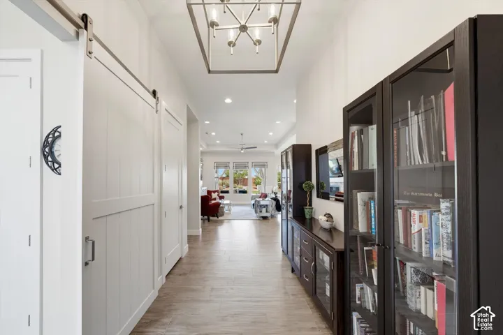 Wide hallway with wood-finish flooring, two white barn doors on a brushed nickel track, and recessed lighting