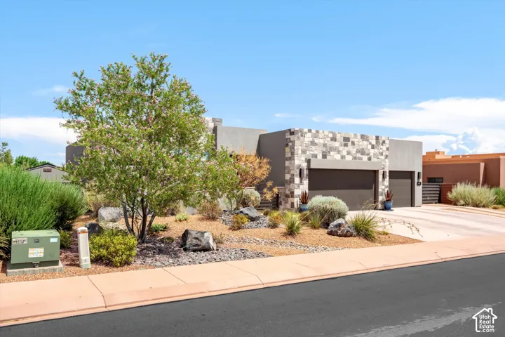 Contemporary architectural style, stone and stucco exterior, two garage doors, and xeriscaped front yard with mature plantings