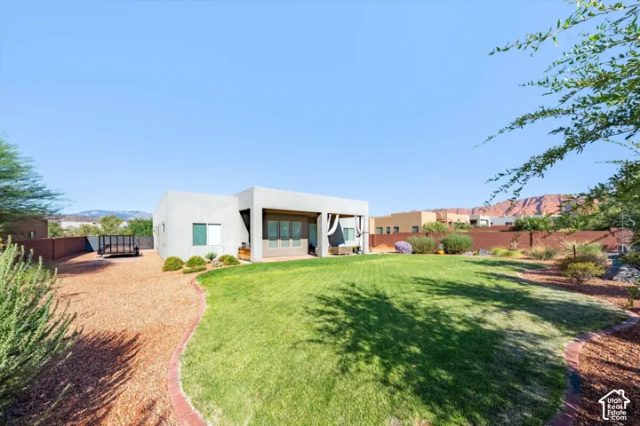 Expansive backyard featuring a green lawn, natural landscaping, and a stucco exterior with multiple windows
