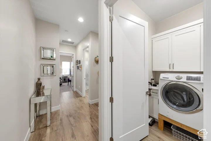 Hallway featuring wood-finish flooring, recessed lighting, and a laundry area with white cabinetry