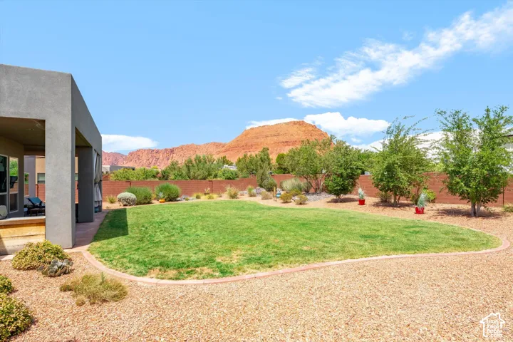 Expansive backyard featuring a manicured lawn, gravel landscaping, a covered patio area, and mature trees